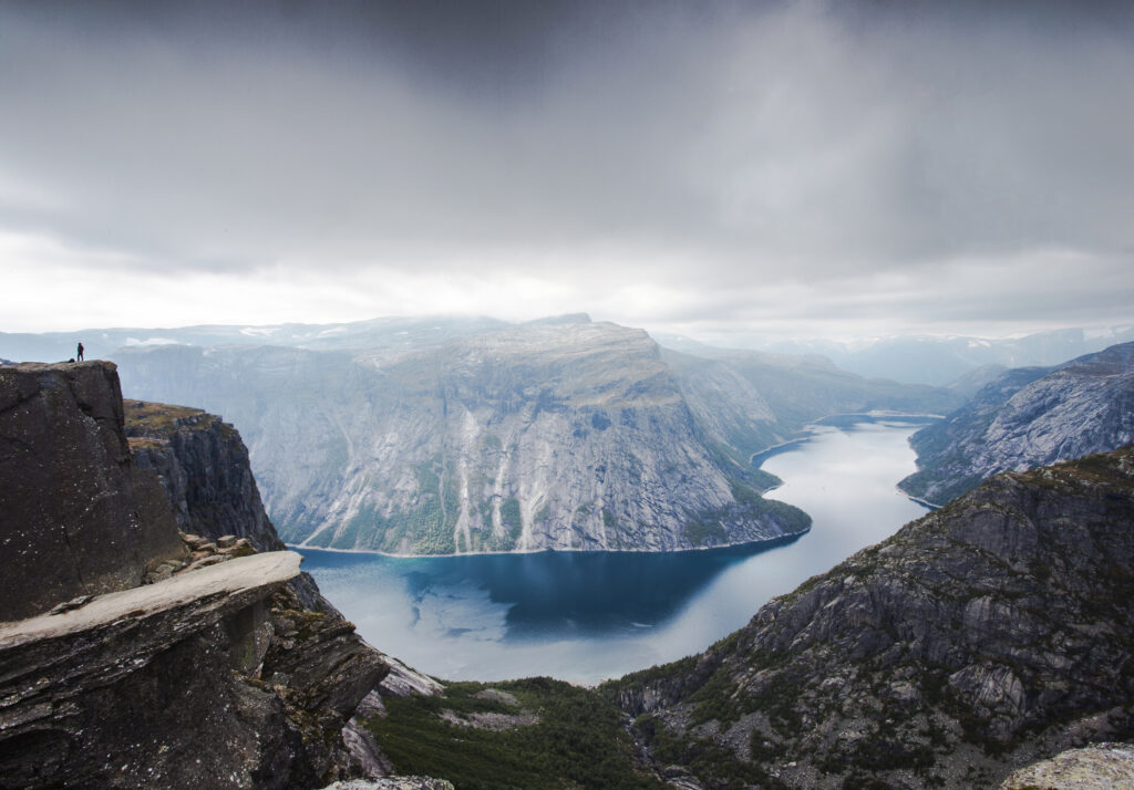 View of Trolltunga cliff and lake between mountains, picturesque landscape, beauty in nature, paradise on Earth, sunny day, Odda, Norway. Cloudy day.