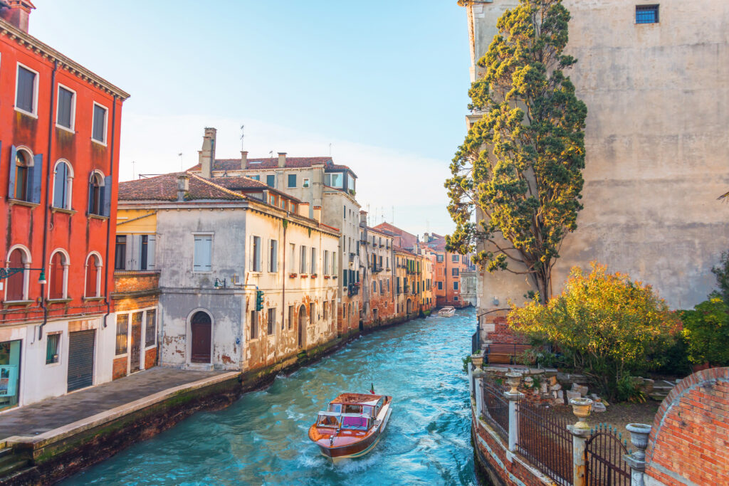 Canal in Venice with a small garden and a tree near the house, on the water a small motor boat