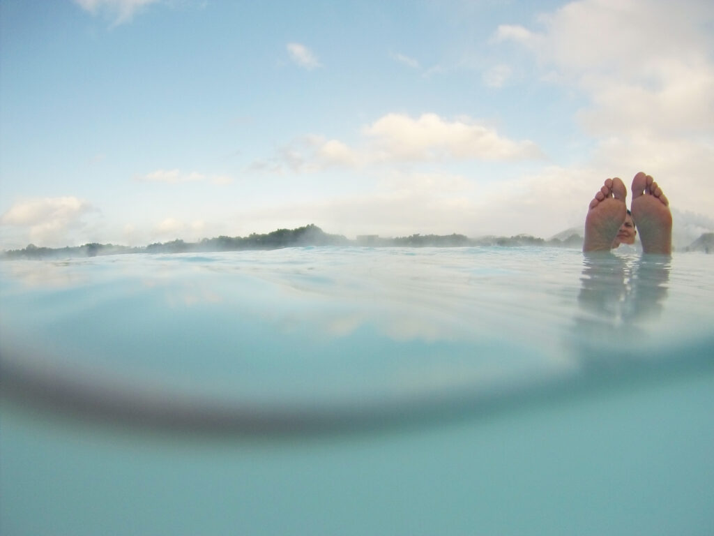 GoPro image: mature woman enjoying life. She is floating in the hot springs water. The photo shows both under and over water line