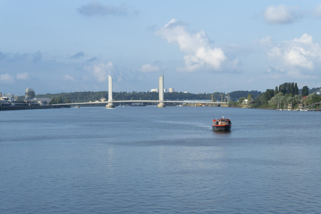 Boat on the Garonne River at Bordeaux, France with the Pont Jacques Chaban Delmas bridge in the background, it is the largest lift bridge in Europe.