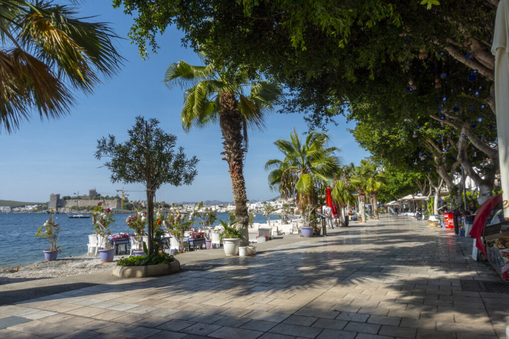 Bodrum, Turkey - November 7, 2019. People sitting and talking each other in beach of Kumbahce bay  in Bodrum. There is a castle in the background.  Mugla Province, Turkey.