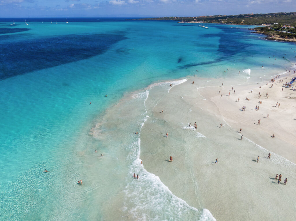 View of people relaxing along the coastline on the beach in Sardinia, Italy.