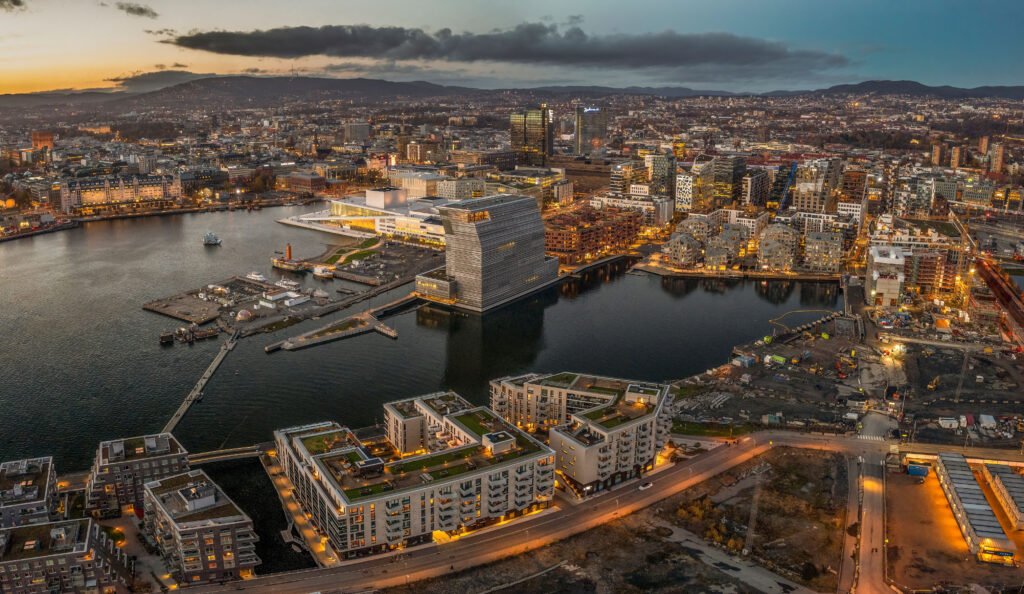 An aerial shot of Oslo at sunset, with lots of buildings and lights, surrounded by sea, Norway