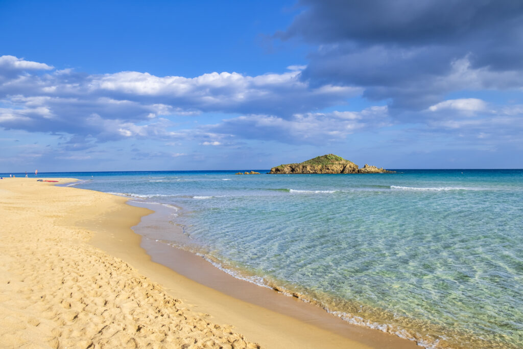 Shallow and crystal clear waters in front of the golden sand beach of Su Giudeu, with an islet easy to reach on foot