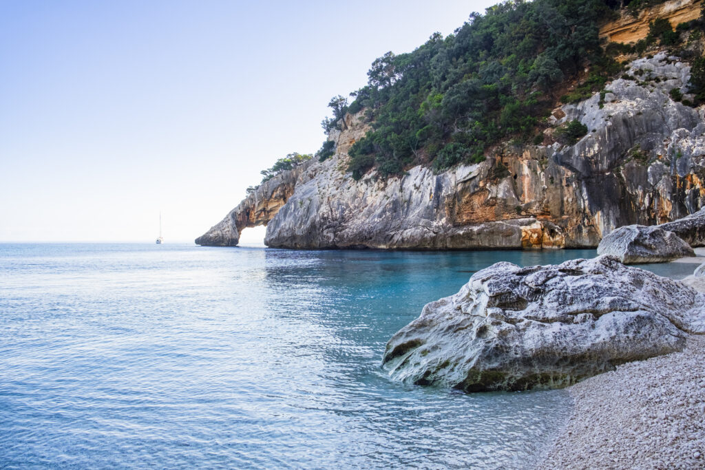 Crystal clear water laps the Cala Goloritzé, a cove of white small pebbles protected by a rugged cliff with a natural arch