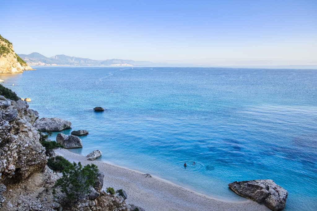 Crystal water laps Cala Goloritzé, a cove protected by a rugged cliff reachable via trekking among Mediterranean scrub in the Supramonte di Baunei