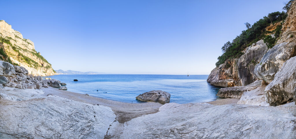 Crystal water laps the Cala Goloritzé, a cove of white small pebbles protected by a rugged cliff with a natural arch (7 shots stitched)