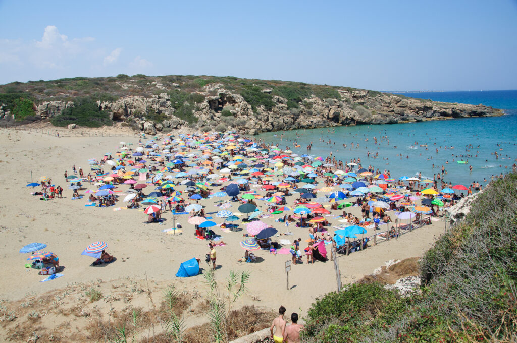 Noto, Italy - August 19, 2013: Calamosche Beach, near Noto in Sicily. Calamosche is situated inside the wonderful reserve of Vendicari, near Noto in Sicily (province of Siracusa).People are taking a bath, swimming, having fun, having relax on the sand. Colored umbrellas are fixed to the ground for many meters from the shoreline.