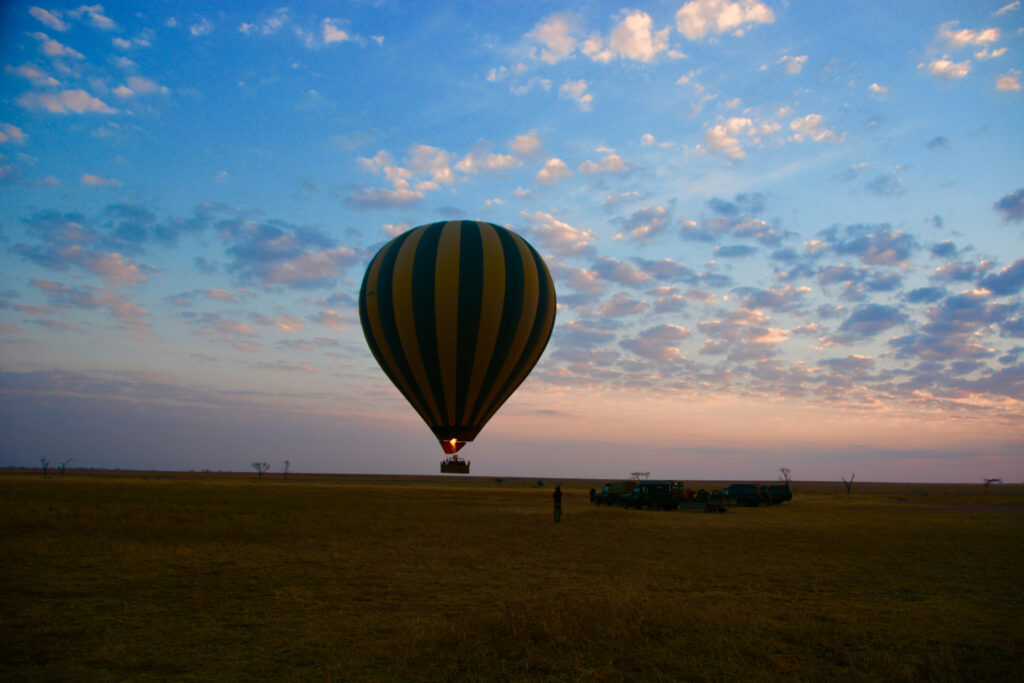 Serengeti, Tanzania - September 17, 2013: hot air balloon taking off during sunrise with cars and people assisting at The Serengeti National Park at dawn.