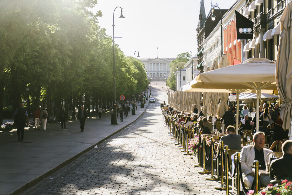 Oslo, Norway - June 15, 2015: Tourists and local people eating in sidewalk cafes on Karl Johans Gate. One of the main shopping streets with lot of outdoor restaurants and shops.