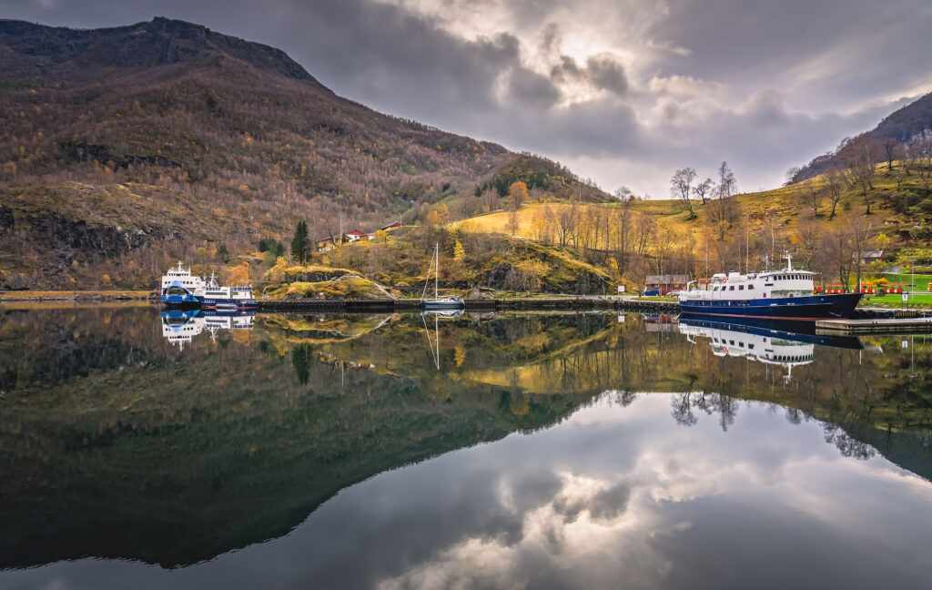 Large passenger ferry and small boat anchored in harbor on the shore in small village Flam, Norway