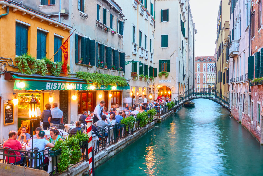 Venice, Italy - June 14, 2018: People at restaurant with tables outdoors near small canal in Venice