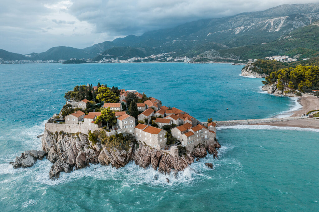 Luxury resort of Sveti Stefan seen from above in the emerald waters of the Adriatic sea and with Budva and mountains in the background.