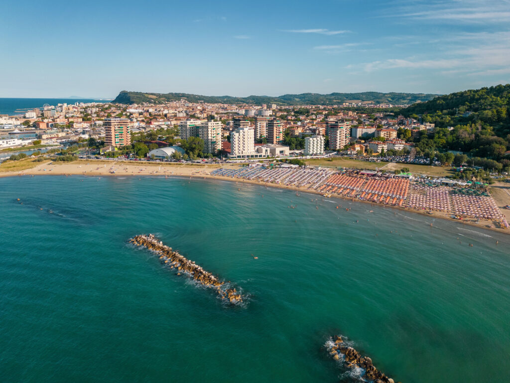 An aerial view of Baia Flaminia in Pesaro with its colored umbrellas and the hotels behind it.